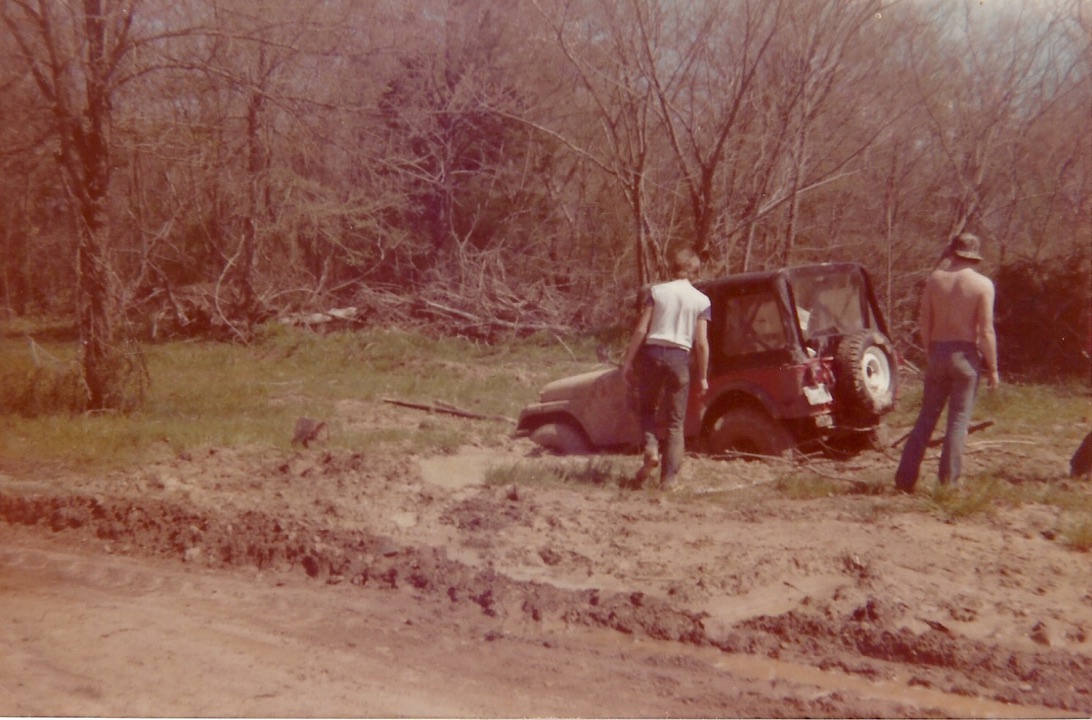 Brad and Donny standing beside a Jeep buried to its axles in a muddy clearing