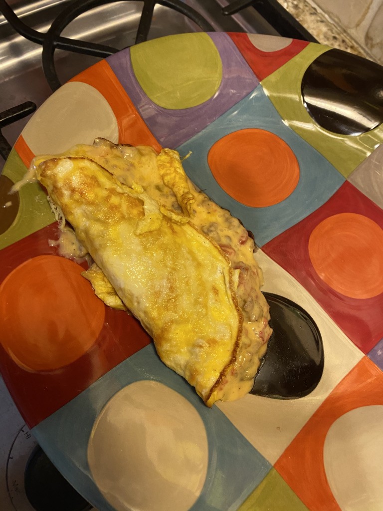 A folded homemade cheese omelet on a colorful plate beside the stove